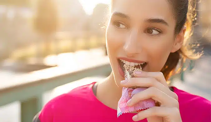 Woman in a bright pink shirt eating a snack bar