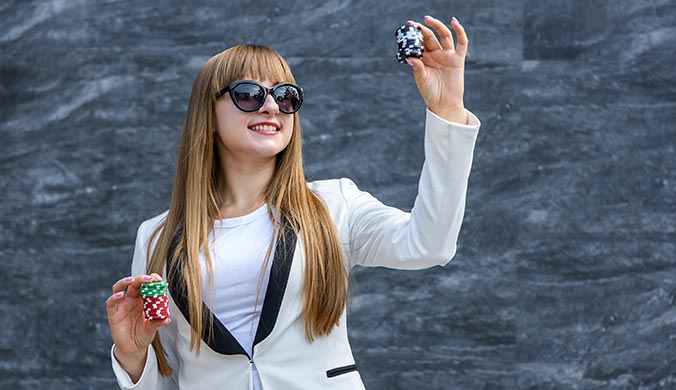 smiling very stylish young woman in white business suit long blond ha holding two dice in one hand and casino chips in the other