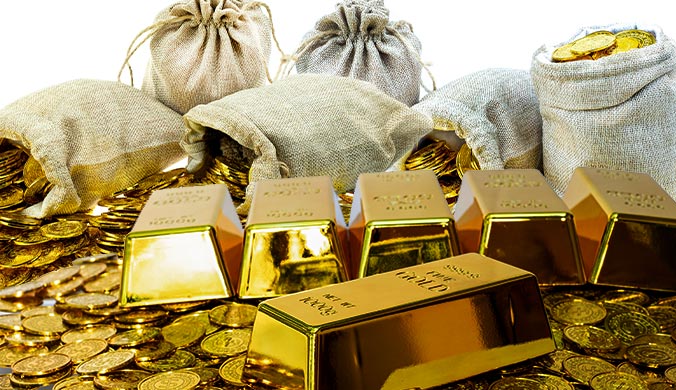 A photo of gold bars, gold coins and bags stuffed with coins spread over a surface with a white background