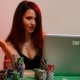 attractive young woman with long dark brown hair playing at an online casino on her laptop with cards and casino chips