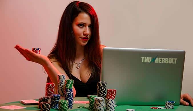 attractive young woman with long dark brown hair playing at an online casino on her laptop with cards and casino chips
