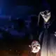 An image of a cloaked and masked man standing by a fire holding a skull during full moon