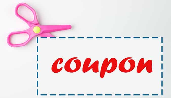A photo of pair of pink scissors cutting the blue perforated edge of white coupon featuring the word coupon in red