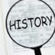 An image of the word history with magnifying glass over an opened book on black background