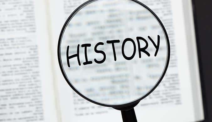 An image of the word history with magnifying glass over an opened book on black background