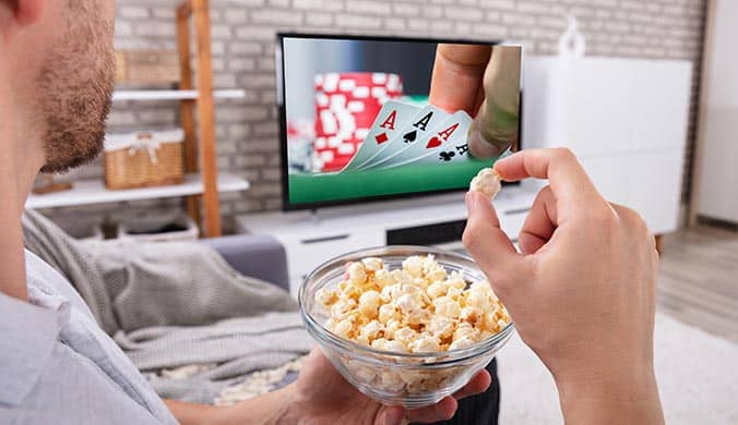 A close-up photo of a man holding a bowl of popcorn watching television at home