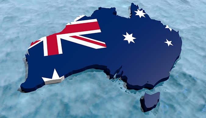 A 3D image of the island continent that is Australia, draped in the Australian flag, against a blue water background