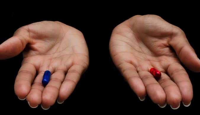 A photo of female hands holding a red and blue pill in each hand, on a dark background